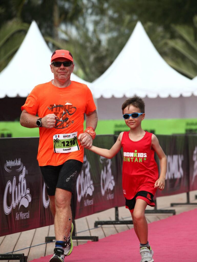 Laurent Labbé approaches an Ironman finish line with his young son, celebrating the finish together, an example of Laurent's desire to keep moving.