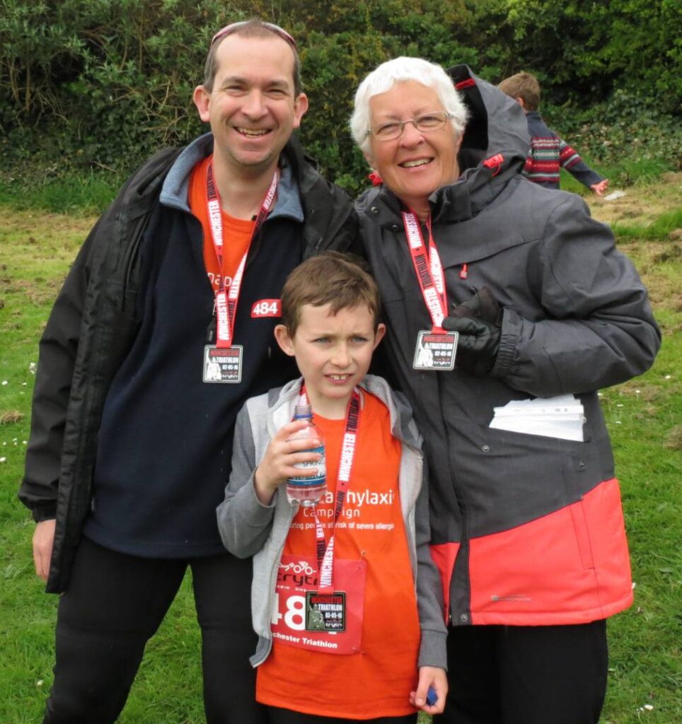 Sue Faulkner smiles with her son and grandson at a triathlon event, illustrating three generations of an active family.
